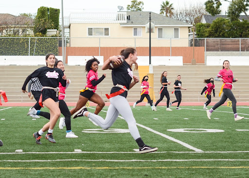 Powderpuff players run towards the endzone, hoping to make a touchdown for their team. Pictured in black shirts were the Blitz Babes, running with the ball, as the Trophy Wives (pictured in pink shirts) followed. Lilly Ramirez-Johnson (12) enthusiastically recounted the game, saying that it was “super fun getting to play a traditional game in front of the school’s audience.”