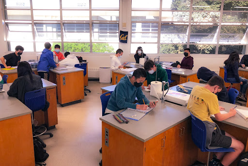 Masked and distanced students take notes in Mr. Collins’ Biology class as he presents a lesson. Just because Omicron hit its peak, it doesn’t mean we’re out of the woods yet: Masks should still be on and distancing regulations should still be in effect. The sooner we all cooperate, the sooner that classes can return to normal. 
