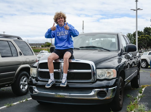 Giving a thumbs up, Matthew Rochford (11) sits on the hood of his 2004 Dodge Ram. “It reflects my personality by just the fact that it runs and I’m a big guy just like my car,” Rochford expressed. 

