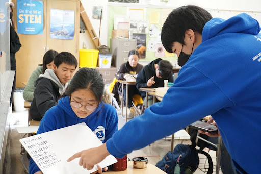 Blazing through round seven of the Pi-Day Competition, contestant Sue-Yan Chin (10) presents her answers consisting of over 70 digits of pi to be verified by Sunwoo Hwang (11). Chin described the competition as tougher than what she remembered from previous experiences: “I was most looking forward to seeing how many digits of pi other people had memorized. Compared to last year, a lot more people came, even some non-math club people, and everyone had memorized a lot more digits of pi.” Photo courtesy of Marina Soen (12).
