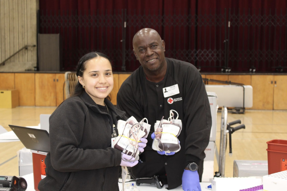 Two American Red Cross workers smile as they display bags of donated blood. They spent the day taking blood and making sure that student donors were healthy enough to participate. Their efforts ensured that the school's blood drive ran safely and smoothly.